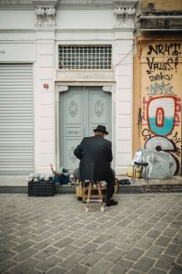 A man shining shoes on a street in Karaköy, vibrant city life with graffiti and classic architecture.